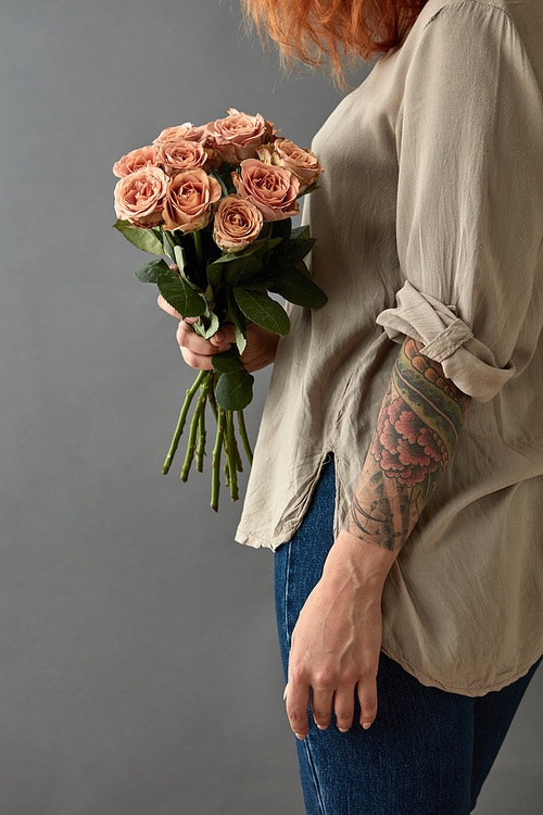 Girl with tattoo on her hand holds a bouquet of beige roses cappuccino, on a gray background. St. Valentine's Day