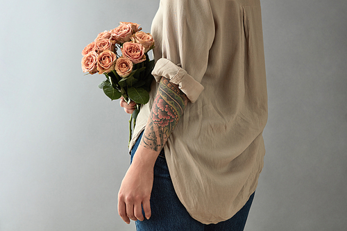 Young woman with a tattoo holds a bouquet of beige roses cappuccino on a gray background. Mother's Day, Valentine's Day