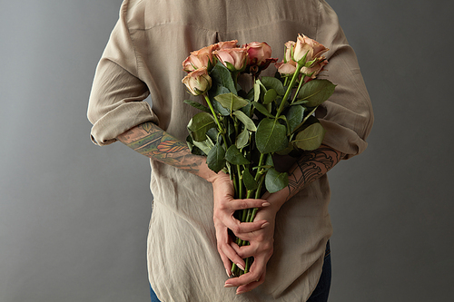 A woman is holding a beautiful bouquet of beige roses cappuccino behind her rear. Against a gray background. Mother's Day,