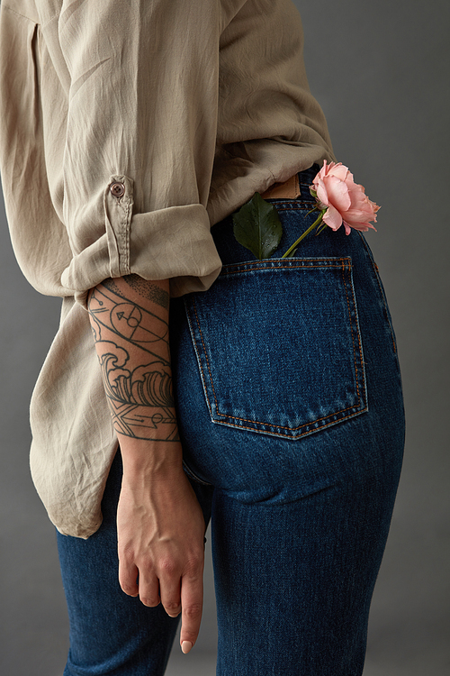 View from the back of a young woman tatoo hand with flower media rose in her pocket. Against a gray background. Mother's Day,