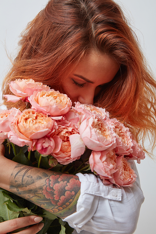 pretty red-haired girl with a tattoo on her arm holding and smell a bouquet of pink roses, valentine's day, mother's day