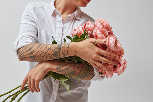 Girl with a tattoo on her hands, holding a bouquet of beautiful pink media roses on a gray background. Mothers Day