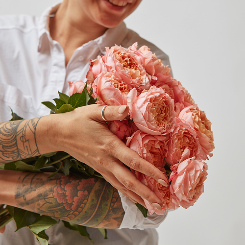 Smiling girl with a tattoo on her hands, holding a bouquet of pink media roses on a gray background. Mothers Day