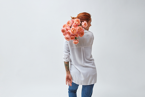 A woman in jeans and a tattoo on her arms, holding a bouquet of pink media roses on her shoulder, mother's day, valentine's day