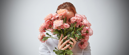A woman hides her face behind a bouquet of pink roses. St. Valentine's Day. Women's Day