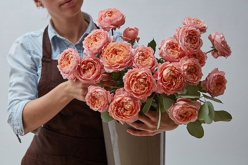 Florist in a brown apron with a vase of pink roses. Girl holding a bouquet of flowers on a gray background.