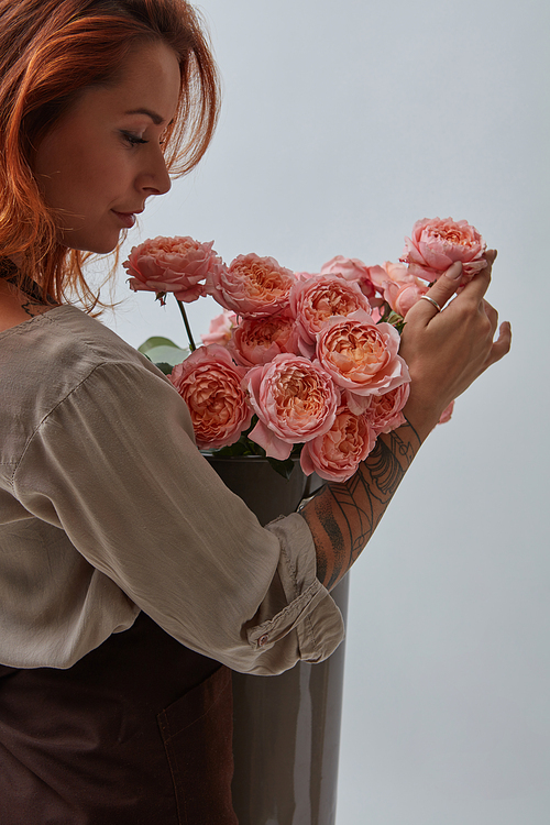 red-haired girl with a tattoo, holding a beautiful bouquet of pink roses in a vase around a gray background with copy space. postcard to valentine's day