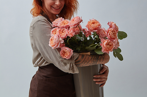 Young red-haired girl with a tattoo holding a bouquet of pink roses around a gray background with copy space. Happy Mother's Day