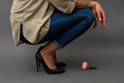 Young stylish girl in jeans, squatting, with pink flower in hands on a dark background with copy space. As a mock-up for Valentine's Day greeting card