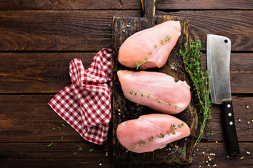 Raw chicken breasts fillets with thyme and spices on wooden cutting board on rustic background copy space directly above