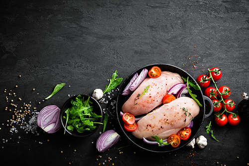 Fresh raw chicken meat, fillet marinated with spices, onion and tomatoes on black background. Top view