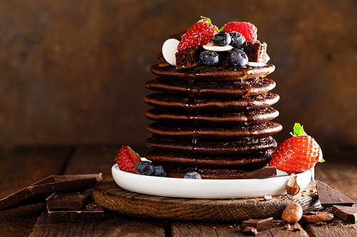 Stack of chocolate pancakes with berries, strawberry, raspberry and blueberry