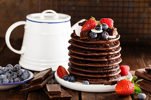 Stack of chocolate pancakes with berries, strawberry, raspberry and blueberry