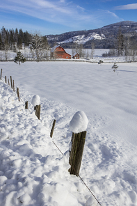 A fence row leads to a red barn in a snow covered field in north Idaho.