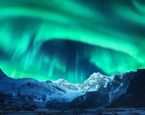 Aurora borealis above the snow covered mountain peak in Norway. Northern lights in winter. Night landscape with green polar lights and snowy mountains. Starry sky with aurora over the rocks. Space