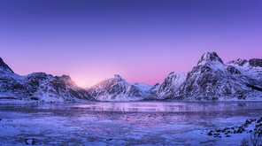 snowy mountains, blue sea with frosty coast, reflection in water and purple sky at colorful  in lofoten islands, norway. winter landscape with snow covered rocks, fjord with ice at night. nature