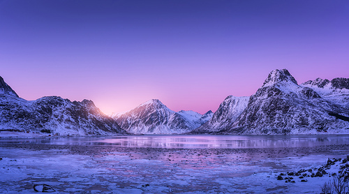snowy mountains, blue sea with frosty coast, reflection in water and purple sky at colorful  in lofoten islands, norway. winter landscape with snow covered rocks, fjord with ice at night. nature
