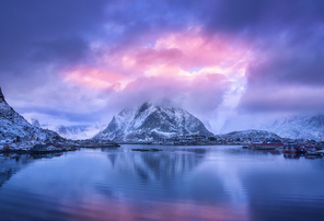 aerial view of snowy mountain, village on sea coast, purple sky at  in winter. top view of reine, lofoten islands, norway. moody landscape with high rocks, houses, rorbu, reflection in water