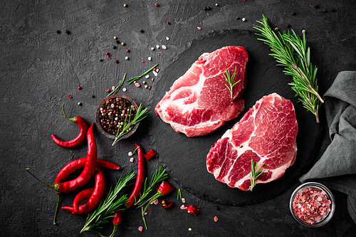 Raw pork meat. Fresh steaks on slate board on black background. Top view