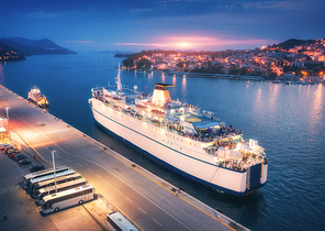 aerial view of cruise ship in port at . landscape with ships and boats in harbour, city lights, buildings, mountains, blue sea at night. top view. luxury cruise. floating liner at harbor at dusk