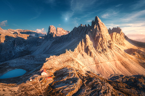 Mountains with beautiful house and church at sunset in autumn. Landscape with buildings, high rocks, lake and blue sky with moon and clouds at dusk. Aerial view of Tre Cime park in Dolomites, Italy