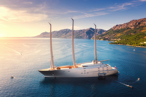 Luxury yacht and blue sea at colorful sunset in summer. Aerial view of big modern sail boat. Top view of beautiful futuristic yacht, lagoon, boats, mountains, clear water, sky. Travel in Adriatic sea