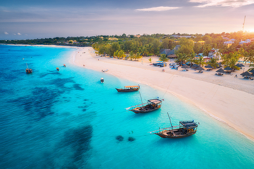 Aerial view of the fishing boats on tropical sea coast with white sandy beach at sunset. Summer holiday on Indian Ocean, Zanzibar. Landscape with boat, palm trees, transparent blue water. Top view