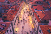 Aerial view of houses with red roofs at night in Dubrovnik, Croatia. Top view of beautiful architecture in old city. City lights, historical centre, buildings, walking people in illuminated streets