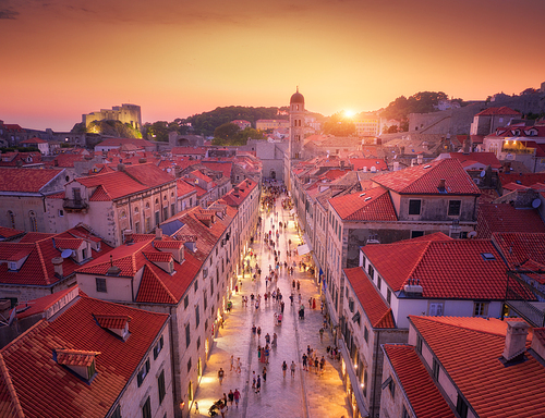 Aerial view of beautiful old city at sunset. Top view of houses with red roofs, city lights, historical centre, architecture, walking people in illuminated streets at night in Dubrovnik, Croatia