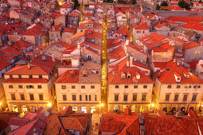 Aerial view of houses with red roofs at night in Dubrovnik, Croatia. Top view of beautiful architecture in old city. City lights, historical centre, buildings, walking people in illuminated streets