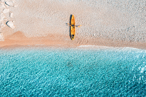 Aerial view of empty sandy beach with yellow canoe, sea coast with transparent blue water in sunny bright day in summer. Travel in Croatia. Top view of boats. Landscape with kayaks at sunset. Travel