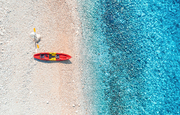Aerial view of empty sandy beach with red canoe, sea coast with transparent blue water in sunny bright day in summer. Travel in Croatia. Top view of boats. Landscape with kayaks at sunset. Travel