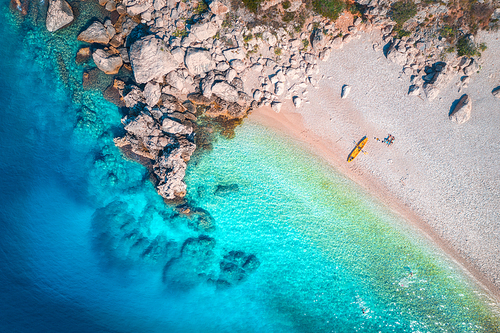 Aerial view of sandy beach with couple and canoe, sea with transparent blue water and rocks in sunny bright day in summer. Travel in Croatia. Top view of boats. Landscape with kayak at sunset. Travel