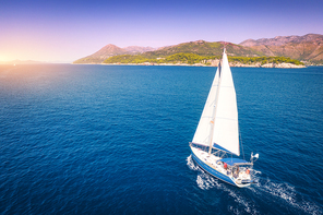 Aerial view of beautiful white sailboat in blue sea at bright sunny summer evening. Adriatic sea in Croatia. Landscape with yacht, mountains, transparent blue water, sky at sunset. Top view of boat