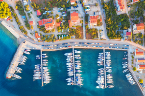 Aerial view of boats and yachts in port in old city at sunset. Summer landscape with houses with orange roofs, motorboats in harbor, clear blue sea, cars on the road. Beautiful architecture. Top view