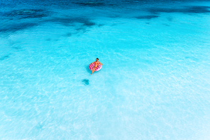 aerial view of a young woman swimming with the pink donut swim ring in the clear blue sea at  in summer. tropical aerial landscape with girl, clear azure water, sandy beach. top view. travel