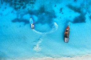 Aerial view of the fishing boats in clear blue sea at sunset in summer. Top view from drone of boat and yacht, sandy beach. Travel in Zanzibar, Africa. Tropical landscape with sailboats, azure water