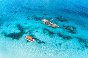 Aerial view of the fishing boats in transparent blue water at sunset in summer. Top view from drone of floating boat in Indian ocean in Zanzibar, Africa. Landscape with yachts in clear sea. Seascape