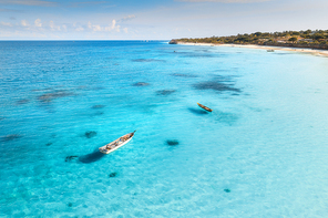 Aerial view of the fishing boat in clear blue water at sunny day in summer. Top view of boat, sandy beach, palm trees. Indian ocean. Travel in Zanzibar, Africa. Colorful landscape with yacht, sea