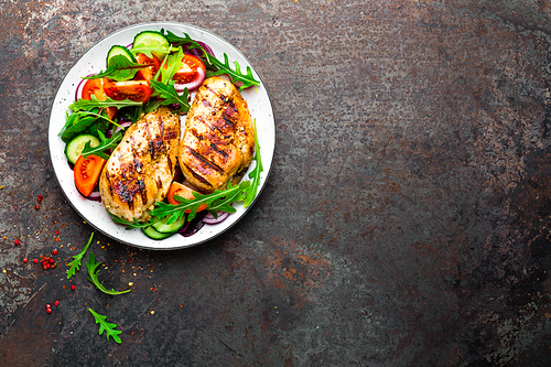 Grilled chicken breast. Fried chicken fillet and fresh vegetable salad of tomatoes, cucumbers and arugula leaves. Chicken meat with salad. Healthy food. Flat lay. Top view. Dark background