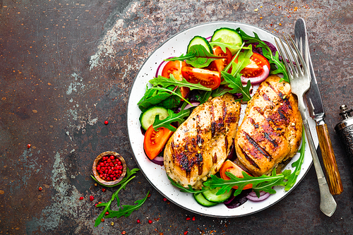grilled chicken breast. fried chicken fillet and fresh  salad of tomatoes, cucumbers and arugula leaves. chicken meat with salad. healthy food. flat lay. top view. dark background