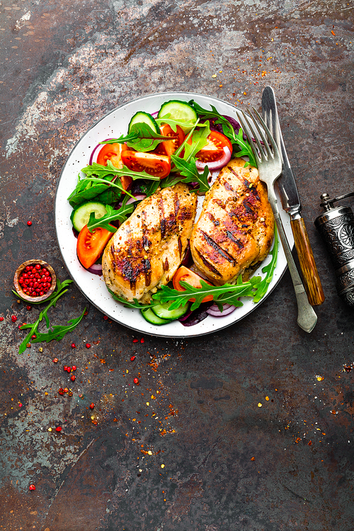 grilled chicken breast. fried chicken fillet and fresh  salad of tomatoes, cucumbers and arugula leaves. chicken meat with salad. healthy food. flat lay. top view. dark background