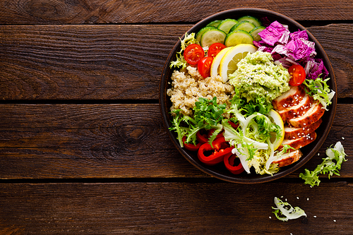 Buddha bowl dish. Healthy balanced lunch with quinoa, grilled chicken meat, lettuce salad, pepper, cucumber, tomato and avocado guacamole with lemon