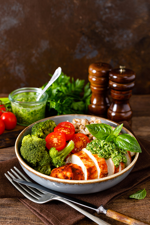 Chicken lunch bowl with broccoli, fresh tomato, pearl barley porridge and basil pesto on wooden rustic background