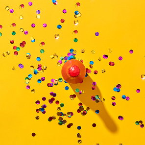 Decorative red painted bottle of wine with hard shadows and colorful confetti on an yellow background, copy space. Top view. Holiday greeting card