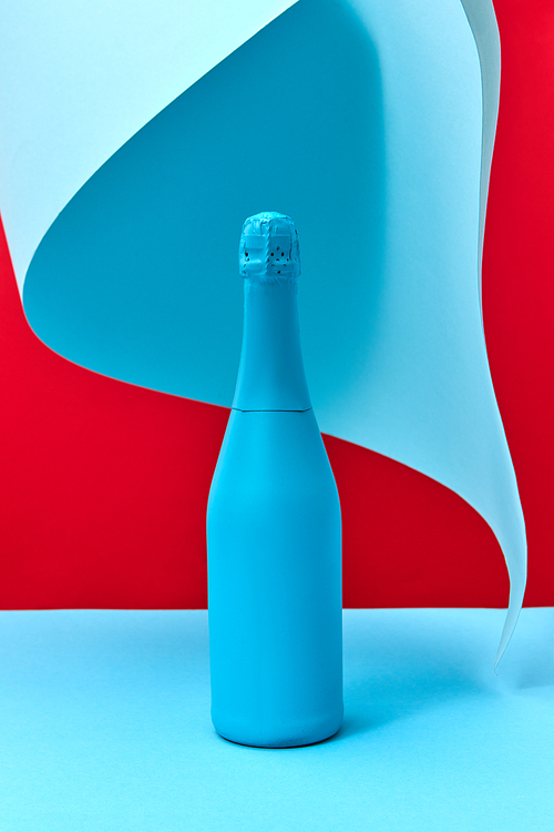 Holiday composition of painted blue wine mock up bottle on a duotone background with folded sheet of blue paper, copy space.