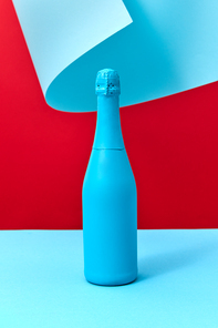 Creative painted blue wine bottle mockup on a duotone background with wavy sheet of blue paper, copy space.