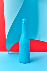 Creative holiday composition with blue painted champagne bottle on a duotone background with curly sheet of blue paper, copy space.