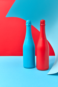 Two creative wine mock-up bottles painted spray red and blue on a duotone wavy background with place for text.