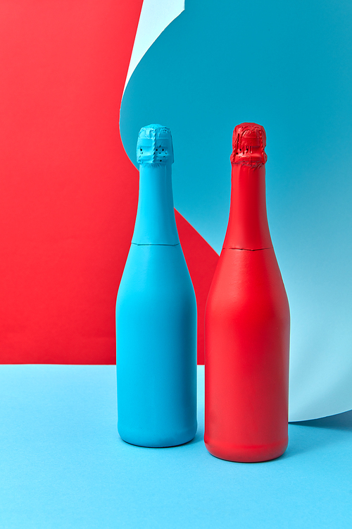 Holiday decorative painted mock-up bottles red and blue on a duotone background with wavy sheet of blue paper behind, copy space.